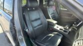 Interior view of a black leather SUV front seats, center console, and gear shifter with the driver’s door open.