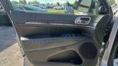 Interior of a car door with a chrome handle and control panel; view of a parking lot visible through the window and side mirror.