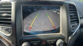 Infotainment screen displaying a rear‑view camera view with colored guide lines (green, yellow, red) and nearby cars while backing up, showing the message 'Check Entire Surroundings'.