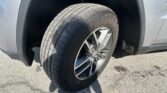 Front wheel and tire of a gray SUV, visible in the wheel well with the fender around it partially shaded by sunlight.