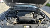 Car hood raised, engine bay visible with battery, hoses, and a V6 engine cover