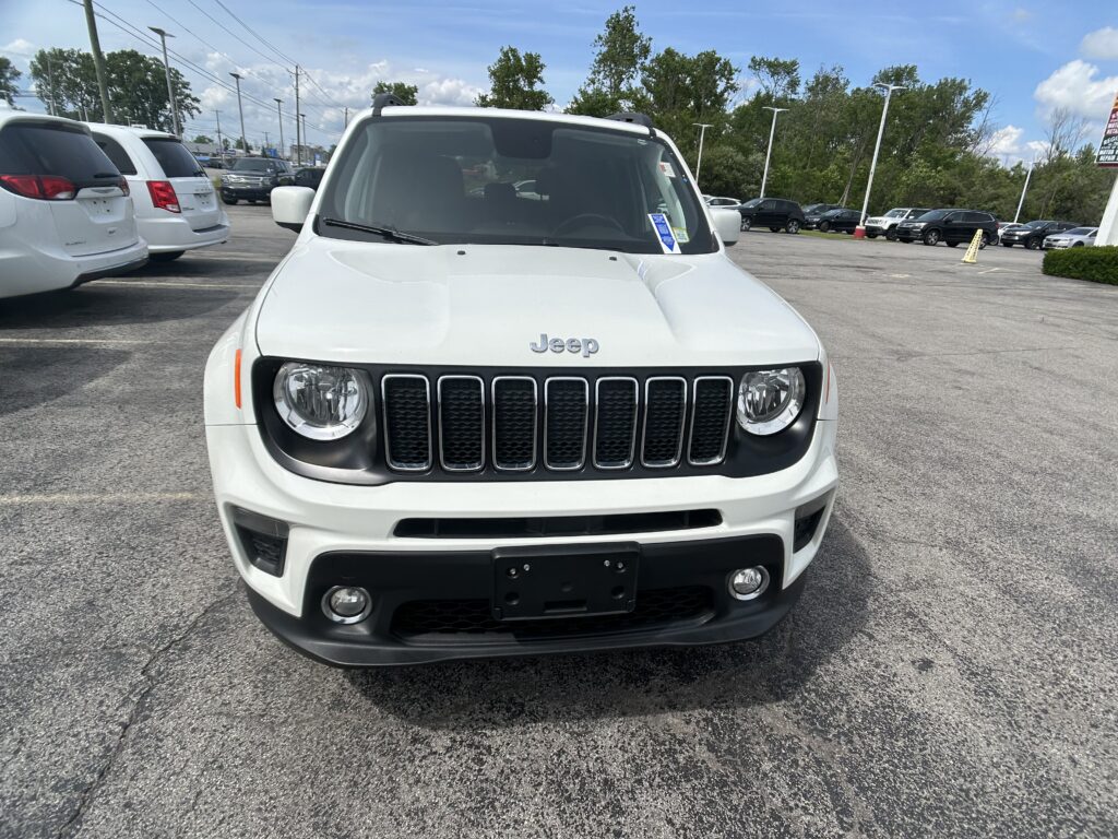 Front view of a white Jeep SUV parked in a car lot on a sunny day, with other vehicles in the background.