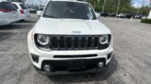 Front view of a white Jeep SUV parked in a car lot on a sunny day, with other vehicles in the background.