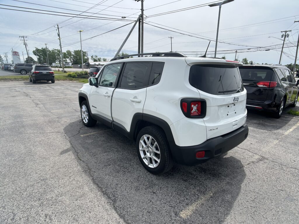 White Jeep SUV in a dealership lot with other cars and power lines overhead