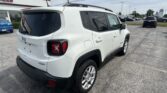 White Jeep SUV photographed from rear-right side in a car lot, with roof rails and dark-tinted rear windows