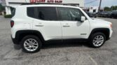 Side view of a white Jeep Renegade SUV with black trim and roof rails parked in a car lot, dealership signage visible in the background.