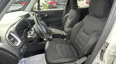 Interior of a car on the driver’s side showing steering wheel, front seats, and dashboard with exterior cars visible through the windows.