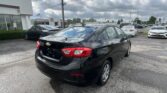 Black Chevrolet sedan in foreground at a car dealership lot with a Toyota dealership building and many parked cars under a cloudy sky?