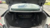 Open car trunk showing a dark, empty cargo area with the rear window reflecting a cloudy sky and parking lot background