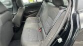 Interior of a dark gray car showing the back seat with headrests, seat belts, and door panel visible; parked cars outside through the windows.