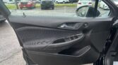 Interior shot of a car door panel and window, with a dealership parking lot visible outside (red pickup, black GMC truck, white cars).