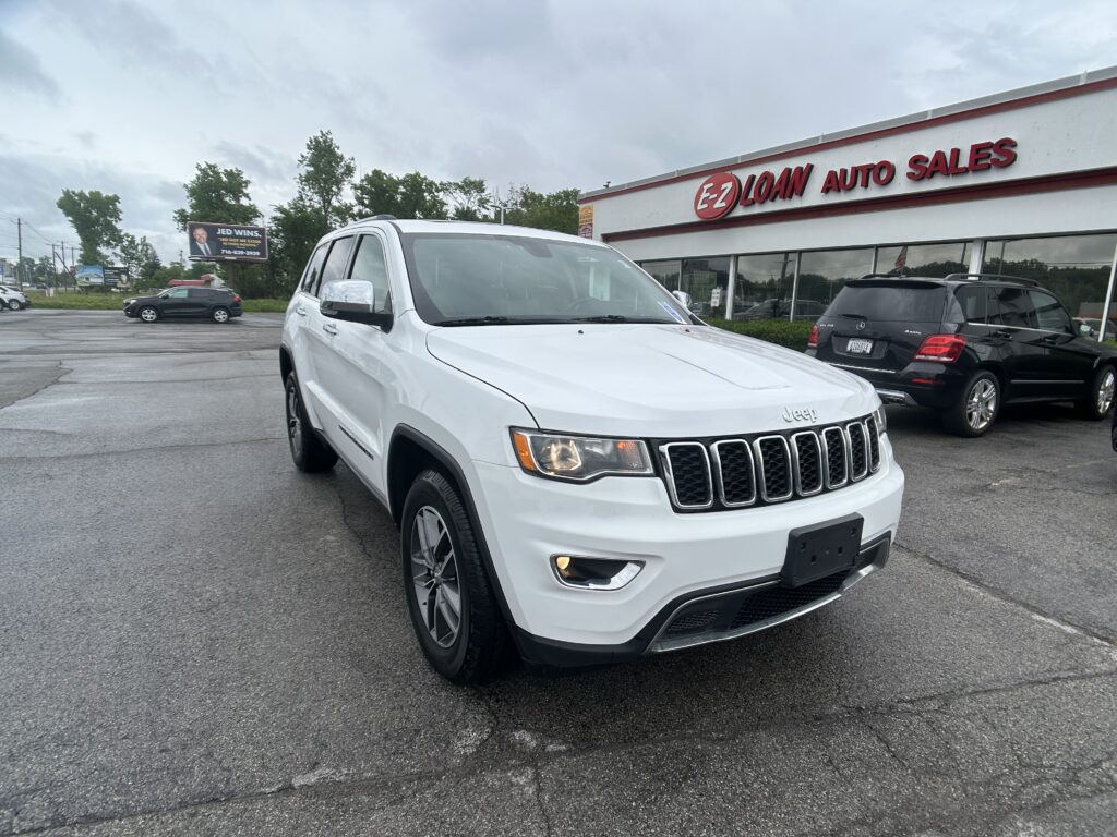 White Jeep SUV parked in a dealership lot in front of EZ Loan Auto Sales building with red sign and other cars nearby.