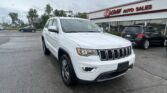 White Jeep SUV parked in a dealership lot in front of EZ Loan Auto Sales building with red sign and other cars nearby.