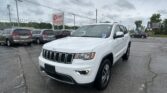 White Jeep SUV in a car dealership lot with other minivans and an Ez Loan sign in the background on a cloudy day.