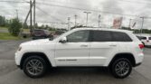 White Jeep Grand Cherokee SUV parked in a lot with utility poles, power lines, and a red EZ LOAN Auto Sales sign in the background
