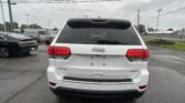 Rear view of a white Jeep SUV in a parking lot on a cloudy day, with other cars and power lines overhead.