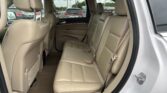 Rear passenger seats in a beige leather SUV interior, seen from the open rear door with headrests and seat belts visible