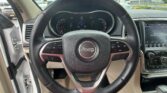 Driver's-seat view of a Jeep: steering wheel with emblem, instrument cluster, and right-side touchscreen inside a car; outside shows a parking lot.
