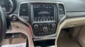 Interior view of a car dashboard with a central touchscreen, climate controls, and cup holders visible between the driver and passenger seats.