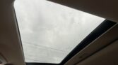 Panoramic car sunroof viewed from inside, with raindrops on glass and cloudy sky outside