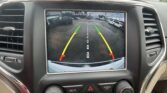 In-car touchscreen showing rear parking camera with colored guide lines (green, yellow, red) and the message 'Check Entire Surroundings'.