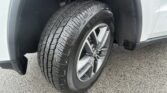 Close-up of a car tire and alloy wheel in a wheel well, showing tread pattern and brake area behind the tire.