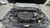 Open hood of a vehicle revealing the engine bay with a prominent V6 engine cover and air intake hose visible at the front.