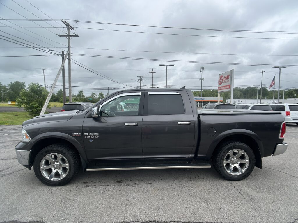 Gray RAM 1500 pickup in a dealership parking lot with a cloudy sky and power lines in the background, viewed from the passenger side.