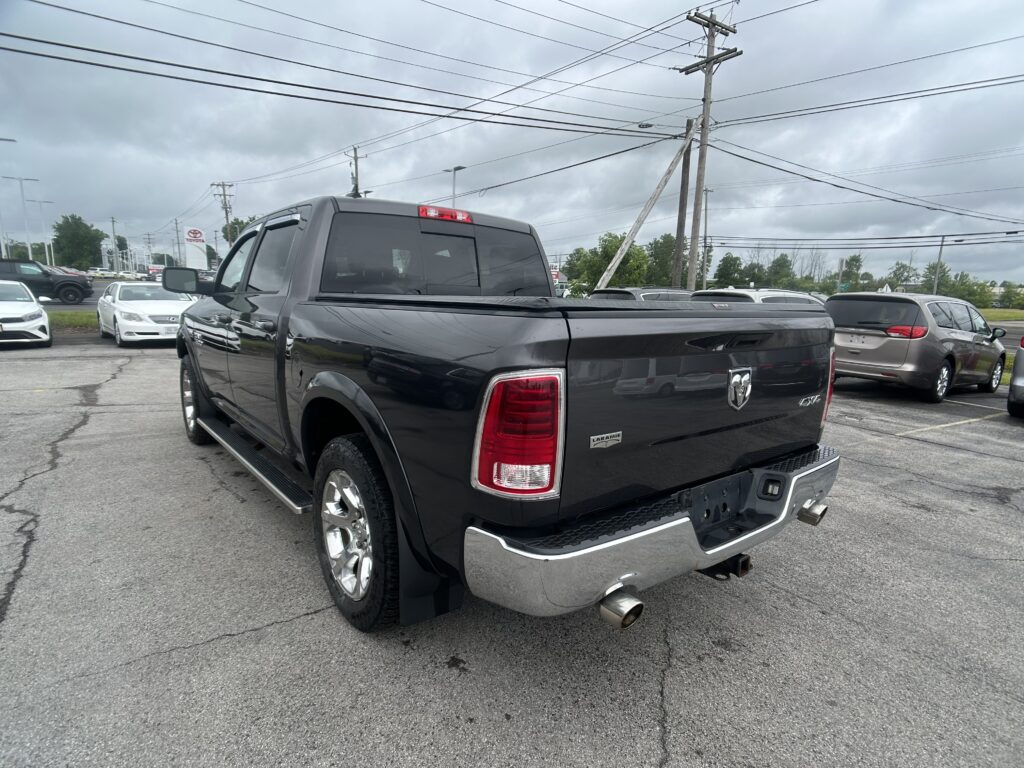 Rear view of a black Ram pickup truck in a car lot, Laramie badge visible, with other cars and power lines in the background.