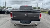 Rear view of a dark gray Ram pickup truck in a parking lot, showing 4x4 badge and dual exhausts on a cloudy day.