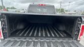 Open pickup truck bed with a black liner and tailgate down in a parking lot on an overcast day, background of other cars and power lines.