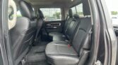 Open rear door view of a vehicle interior with black leather seats and three-seat belts in the back row.
