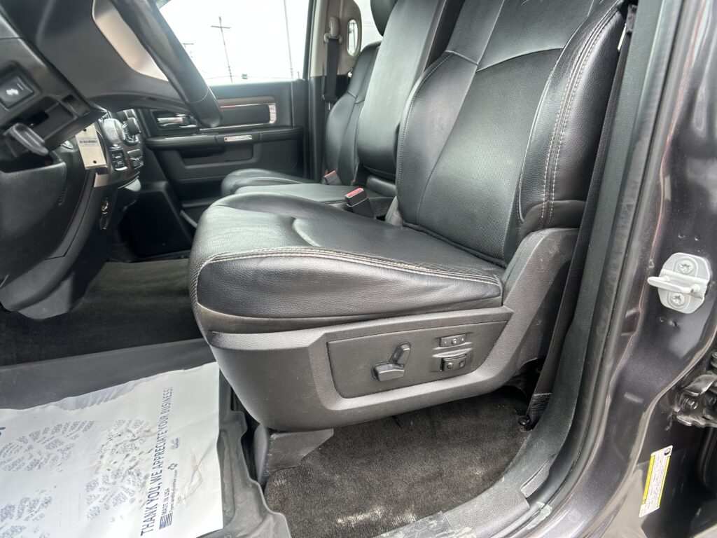 Interior of a black-leather seated car, view from the open front passenger door showing the driver’s seat, steering wheel, and dashboard.