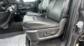 Interior of a black-leather seated car, view from the open front passenger door showing the driver’s seat, steering wheel, and dashboard.