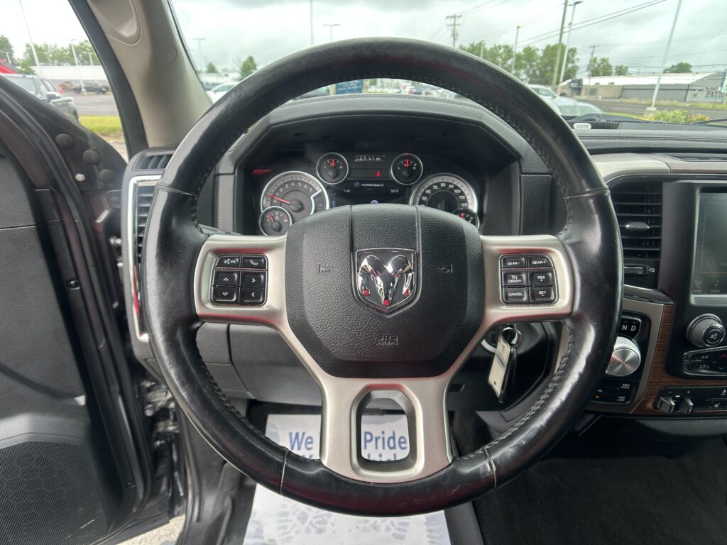 Steering wheel and dashboard view from the driver’s seat in a Ram truck, with instrument gauges and center console visible; parking lot outside through the windshield.
