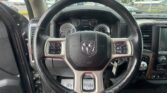 Steering wheel and dashboard view from the driver’s seat in a Ram truck, with instrument gauges and center console visible; parking lot outside through the windshield.