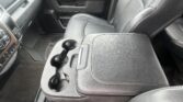 Front interior of a vehicle showing a leather center console with multiple cup holders and adjacent passenger seat.