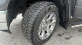 Close-up of a rugged tire on a chrome wheel mounted on a gray pickup, with fender and running board visible. 1st tire close-up, side view.