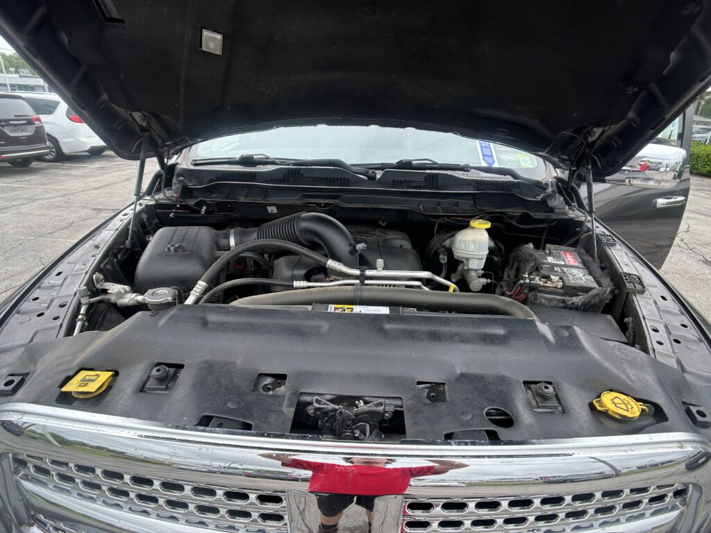 Open hood of a black pickup revealing the engine bay with hoses, the air intake, and a battery on the right side