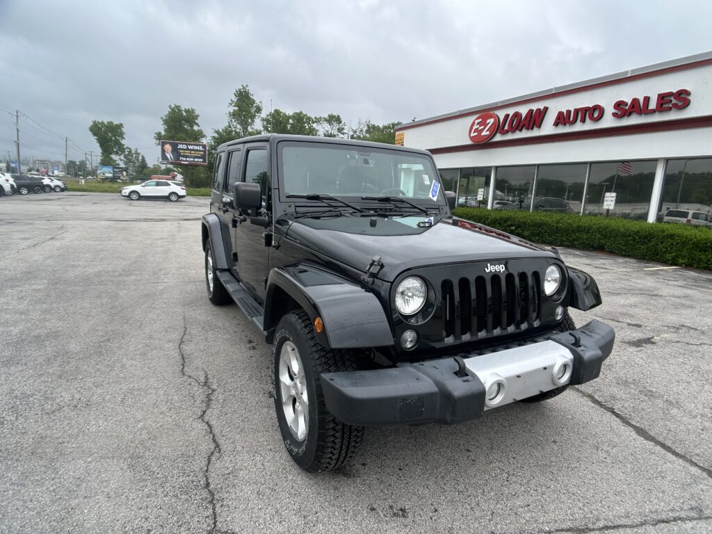 Black Jeep Wrangler in a dealership parking lot with the EZ Loan Auto Sales building in the background; cloudy sky above.