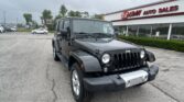 Black Jeep Wrangler in a dealership parking lot with the EZ Loan Auto Sales building in the background; cloudy sky above.