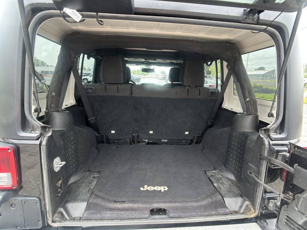 Open rear of a Jeep showing the cargo area with back seats upright and a black floor mat bearing the Jeep logo