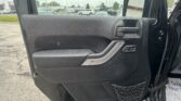 Close-up of a car door interior with a textured black panel, silver handle, and a net pocket; rainy parking lot visible outside.