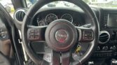 Close-up of Jeep steering wheel from the driver’s seat, with the instrument cluster (speedometer/tachometer) behind and center console visible across the dashboard.