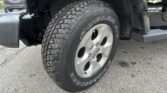 Close-up of a rugged all-terrain tire mounted on a silver wheel on a black Jeep Wrangler Sahara Unlimited, showing tread and fender.