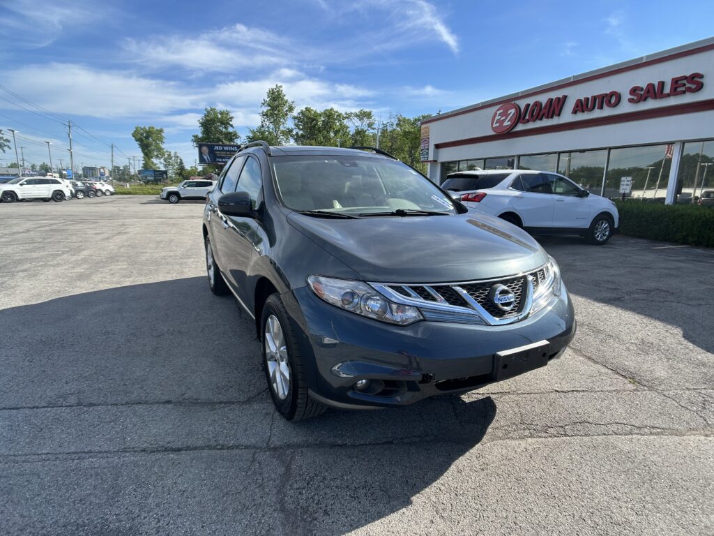 Silver Nissan SUV in foreground at a used car lot with EZ Loan Auto Sales building and blue sky behind.