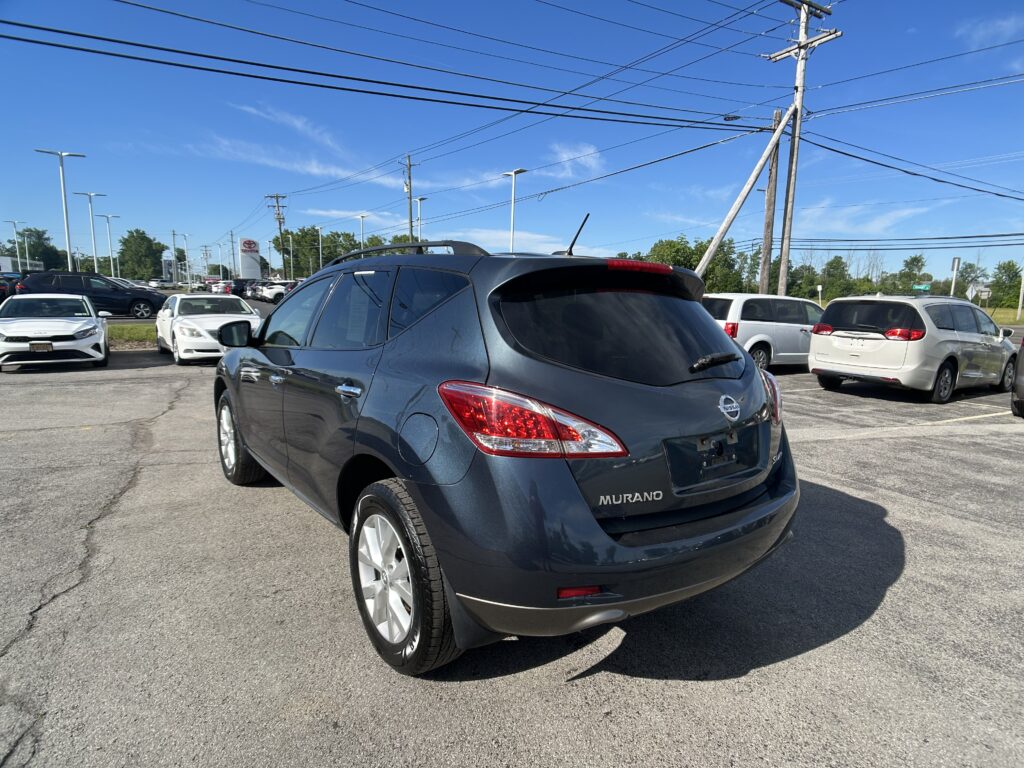 Rear view of a dark blue Nissan Murano in a car dealership lot, with other cars and power lines overhead.