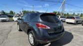 Rear view of a dark blue Nissan Murano in a car dealership lot, with other cars and power lines overhead.