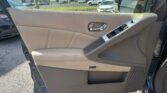 Interior of a tan car door with chrome handle and window controls, dealership lot visible through the window outside.