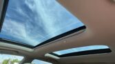 View up through a large panoramic sunroof: blue sky with wispy clouds, beige car interior surrounding.